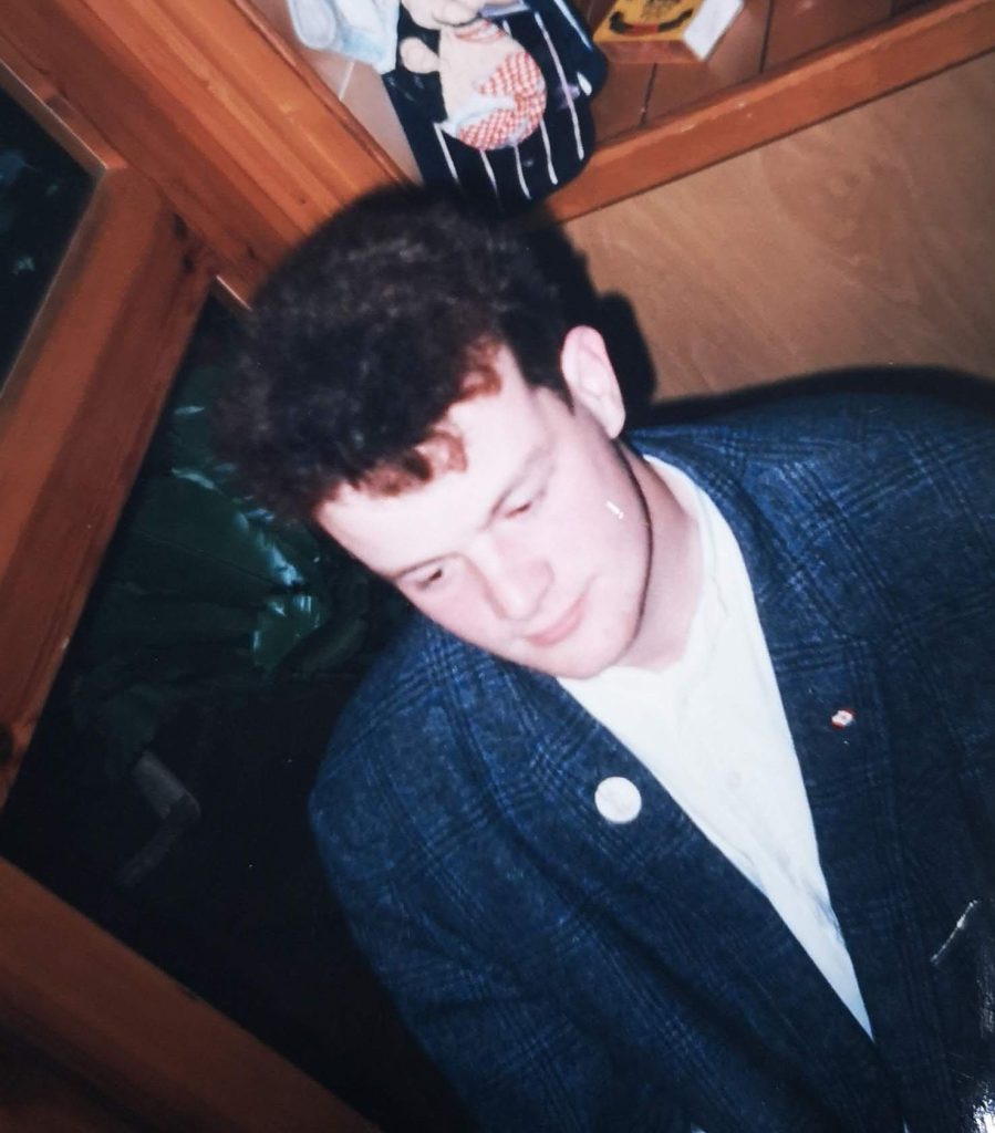 A photograph of the author in the mid to late 1980s. Wearing a dark suit jacket with some badges on it that I can't see clearly.