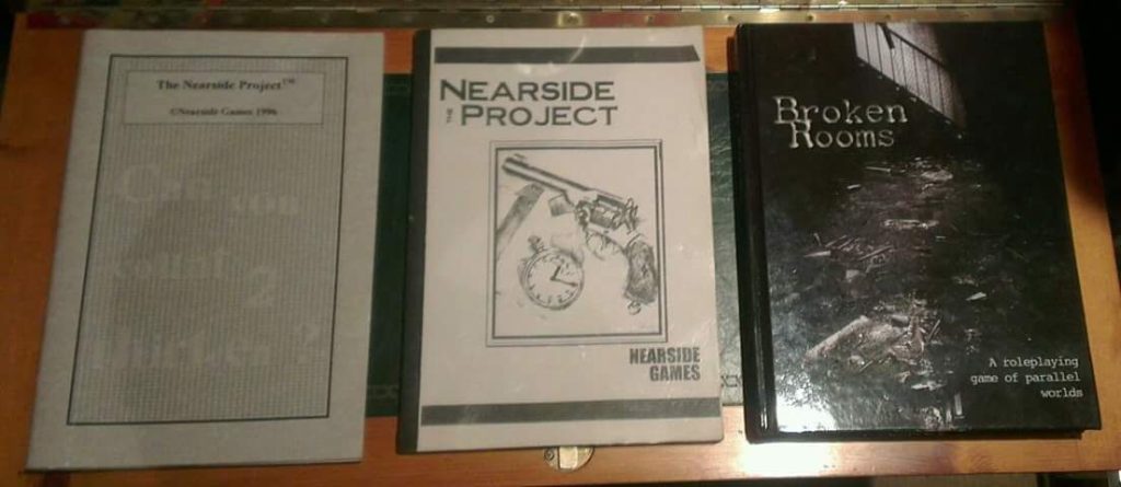 Photograph of three variations of the Nearside Project RPG that became Broken Rooms. Left to right, the initial Nearside Project release from 1996, then a small press style bound copy from 'Nearside Games' - not sure when exactly - then the iirc 2012 hardcover edition of Broken Rooms